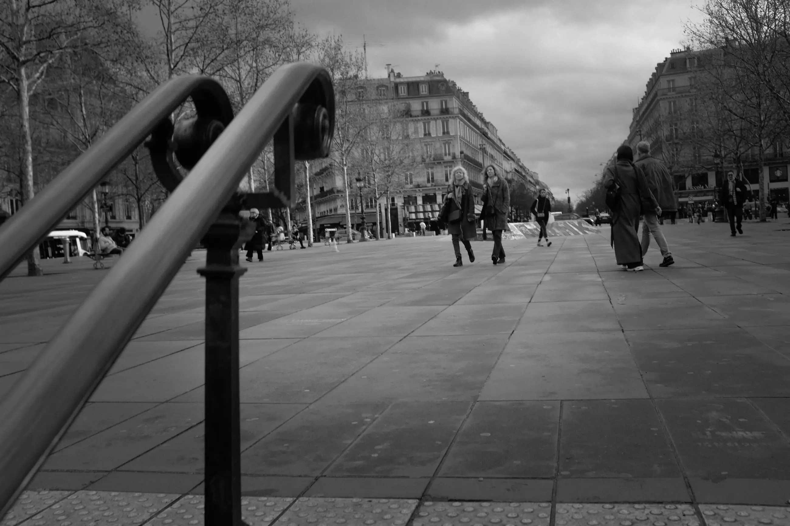 A curved railing in the foreground, pedestrians crossing the Place de la République