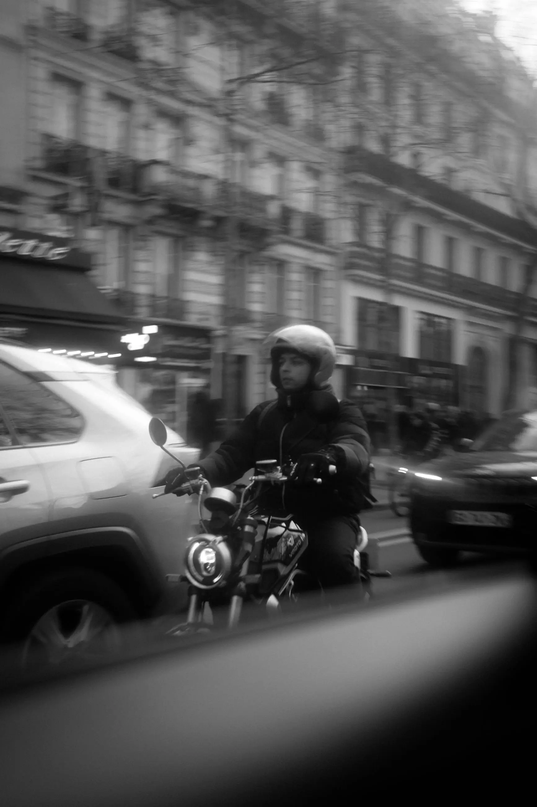 A motorcyclist in a white helmet alongside the taxi on a Paris boulevard