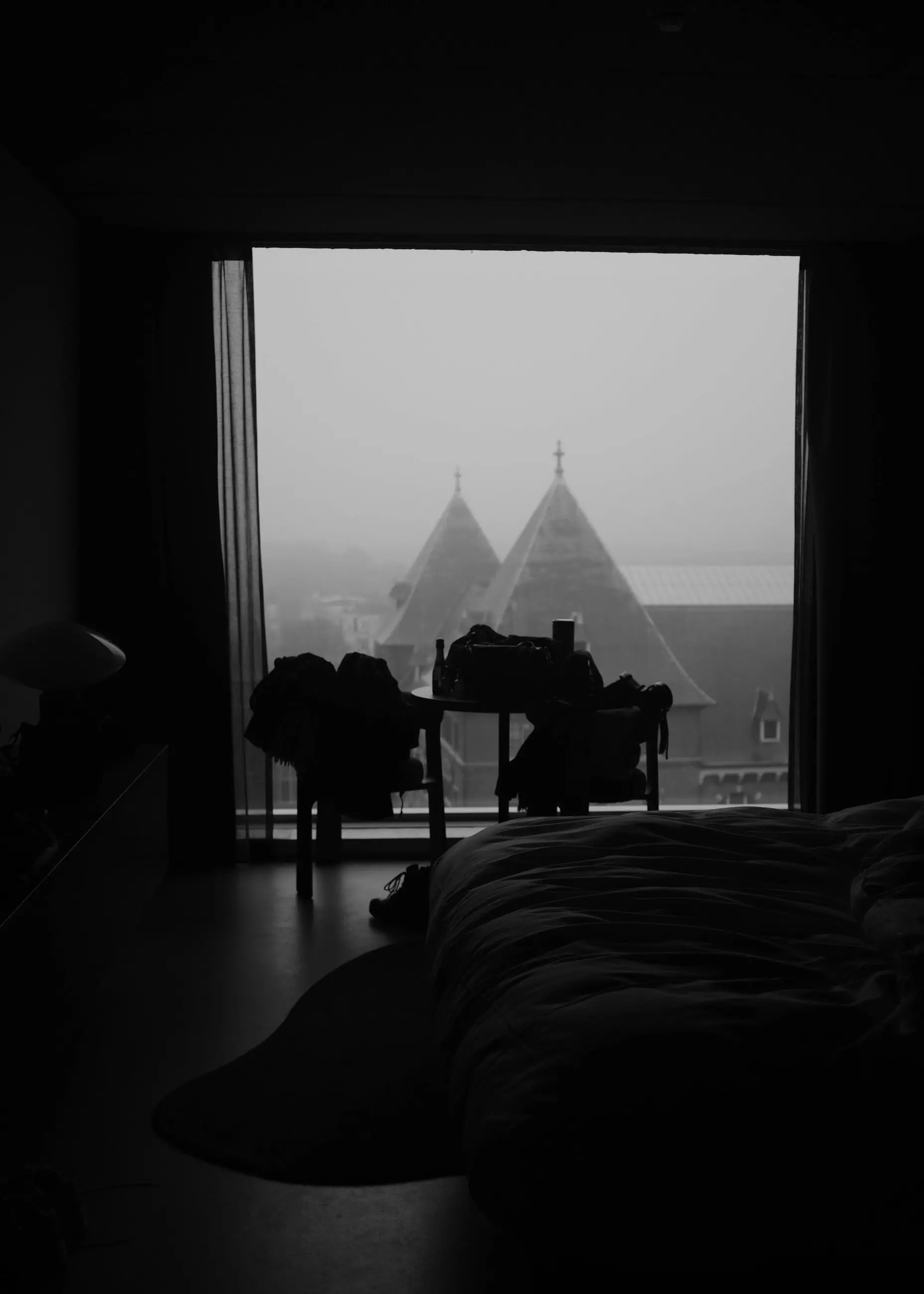 A hotel room window onto misty rooftops, an unmade bed in the foreground