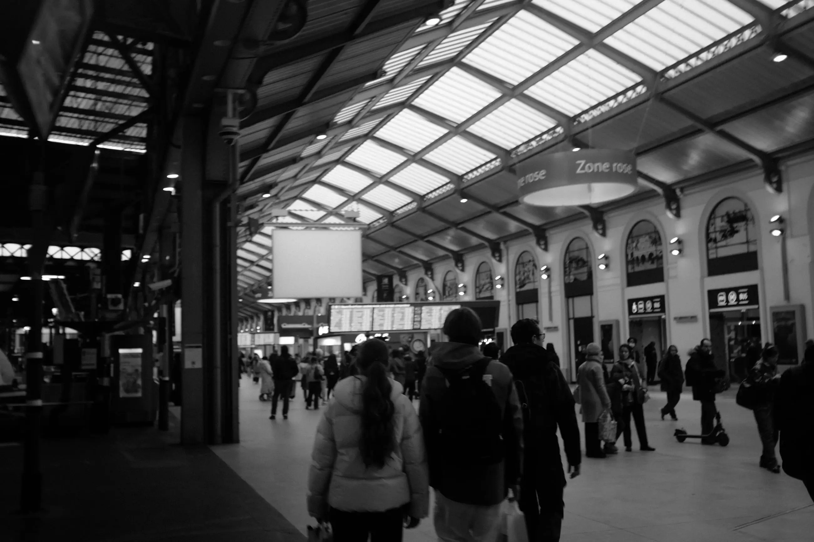 Passengers crossing a glass-roofed station concourse, seen from behind