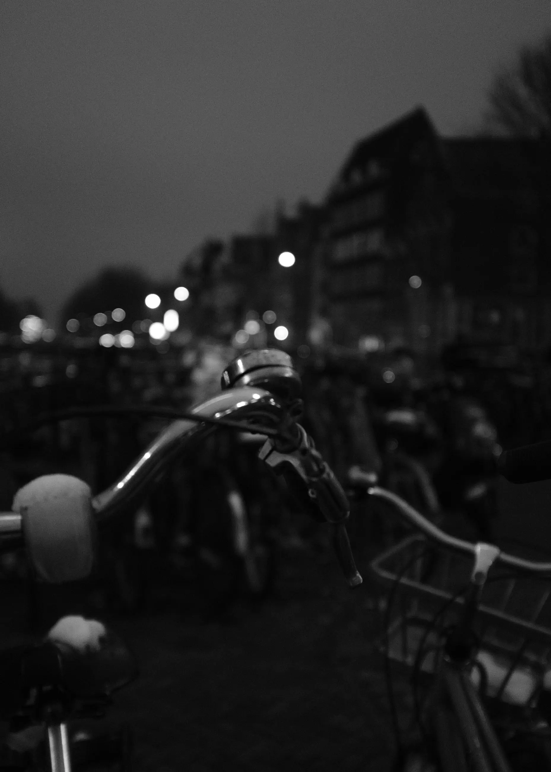Handlebars of parked bikes, lights blurred behind
