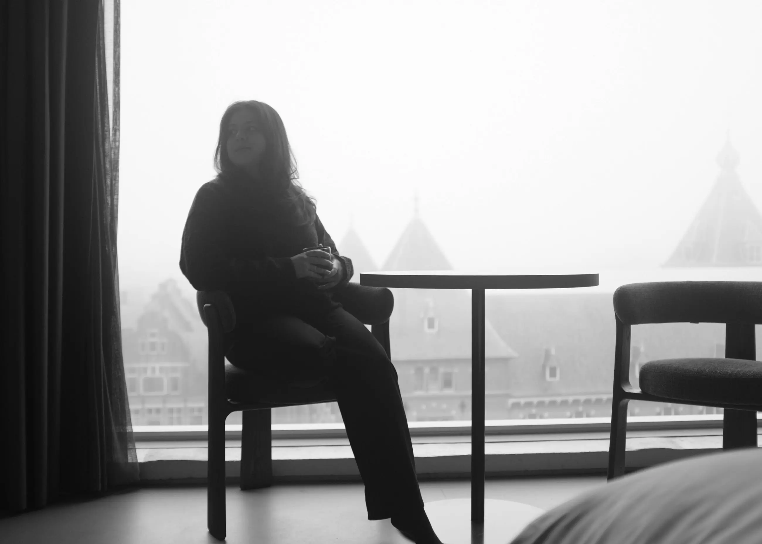 A woman in silhouette on a chair, pointed roofs fading into fog