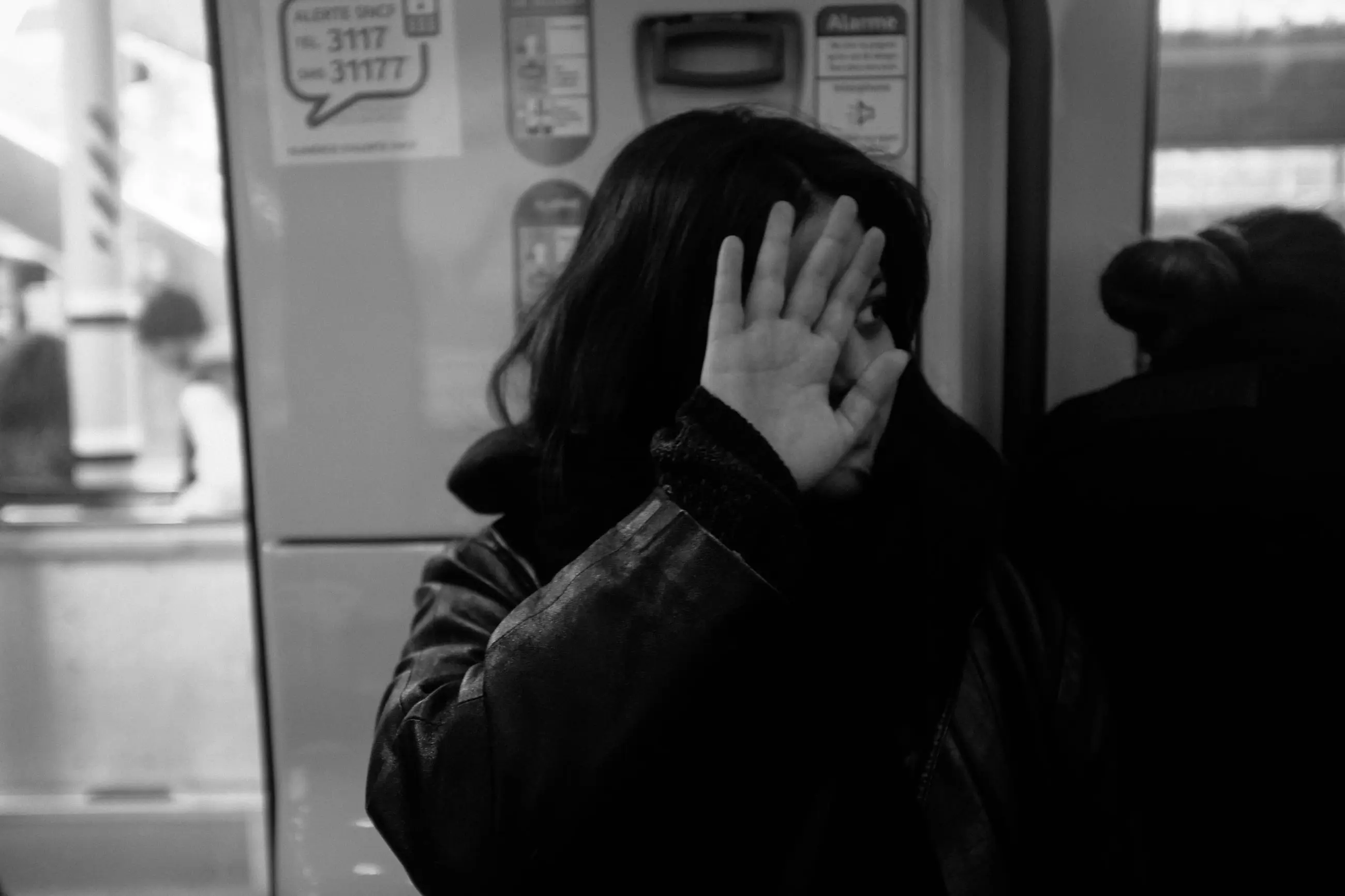 A woman shielding her face with her hand behind a metro door window