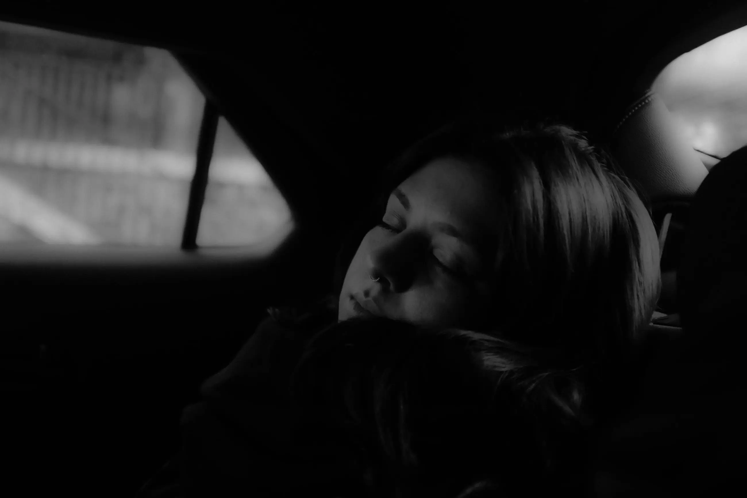 A woman asleep against the seat, the taxi window bright behind her