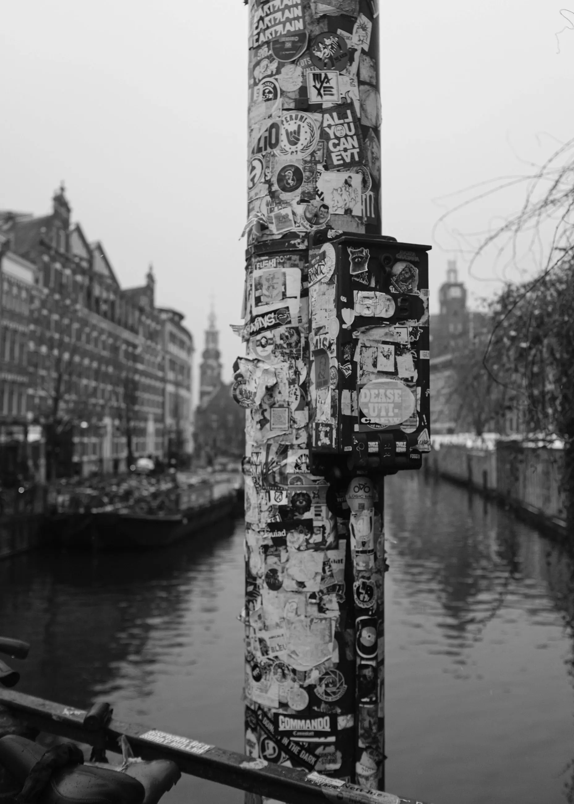 A lamp post covered in stickers above a canal