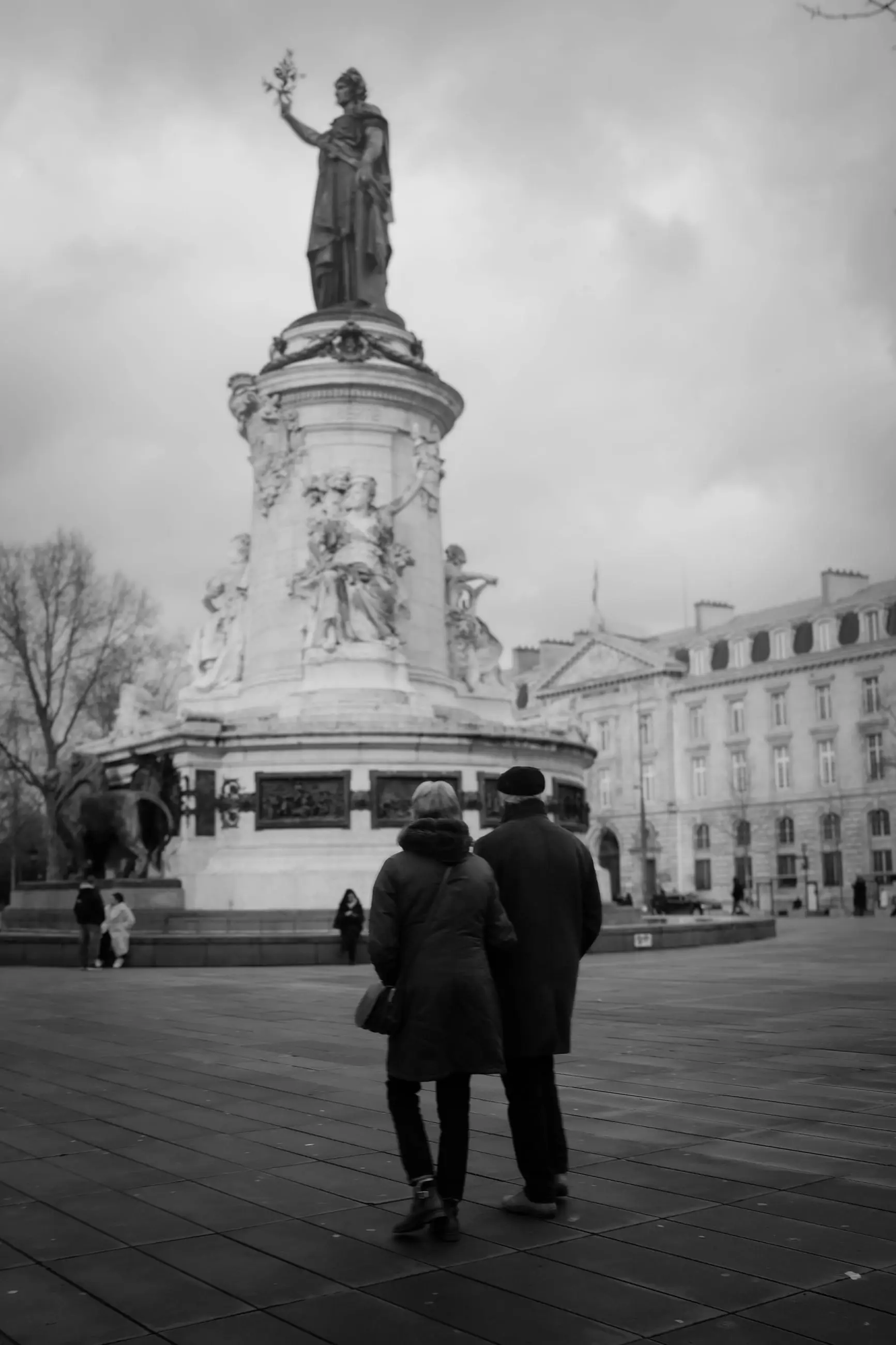 Two pedestrians walk toward the statue of Marianne on the Place de la République