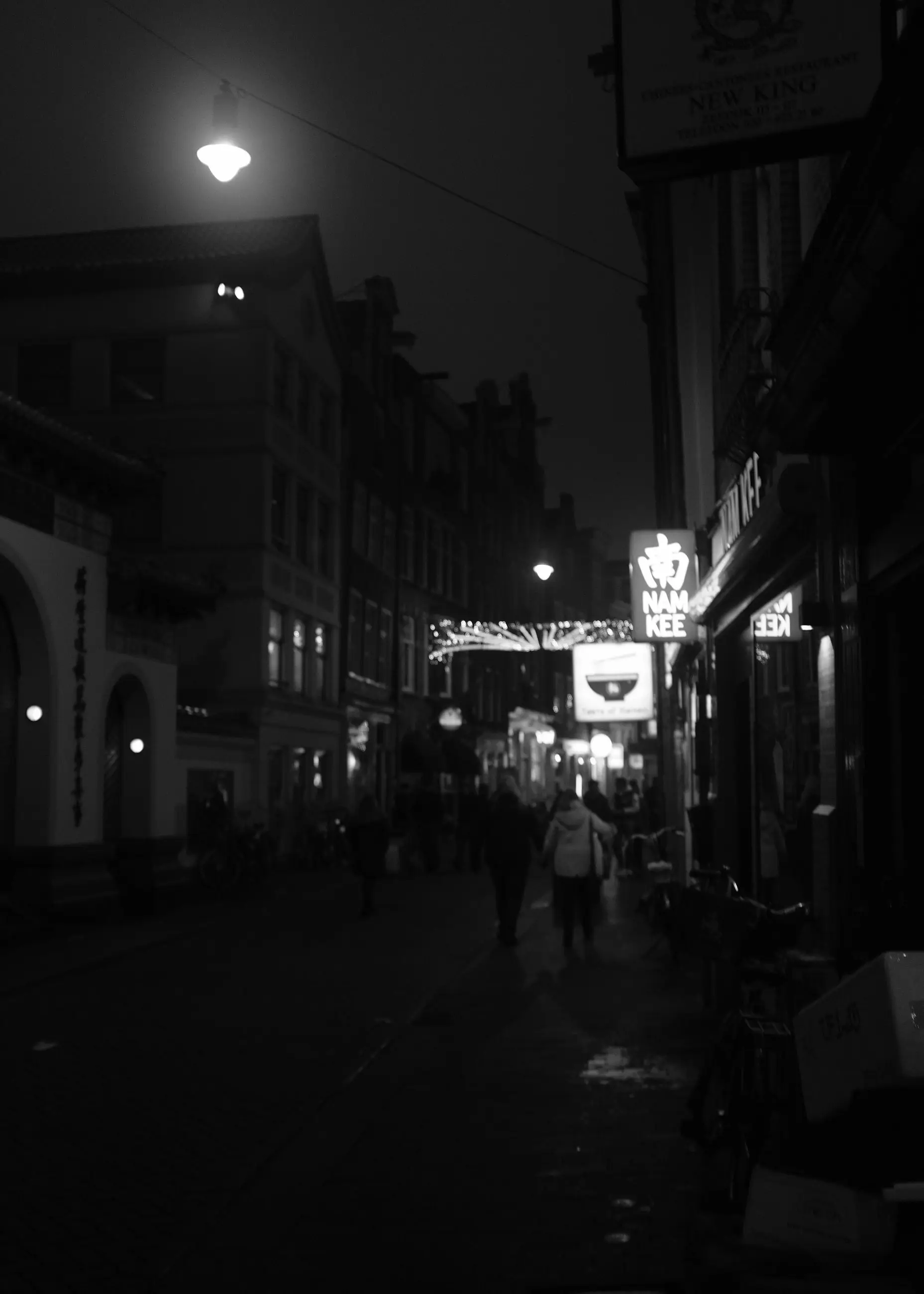 A dark street with a lamp and distant lights