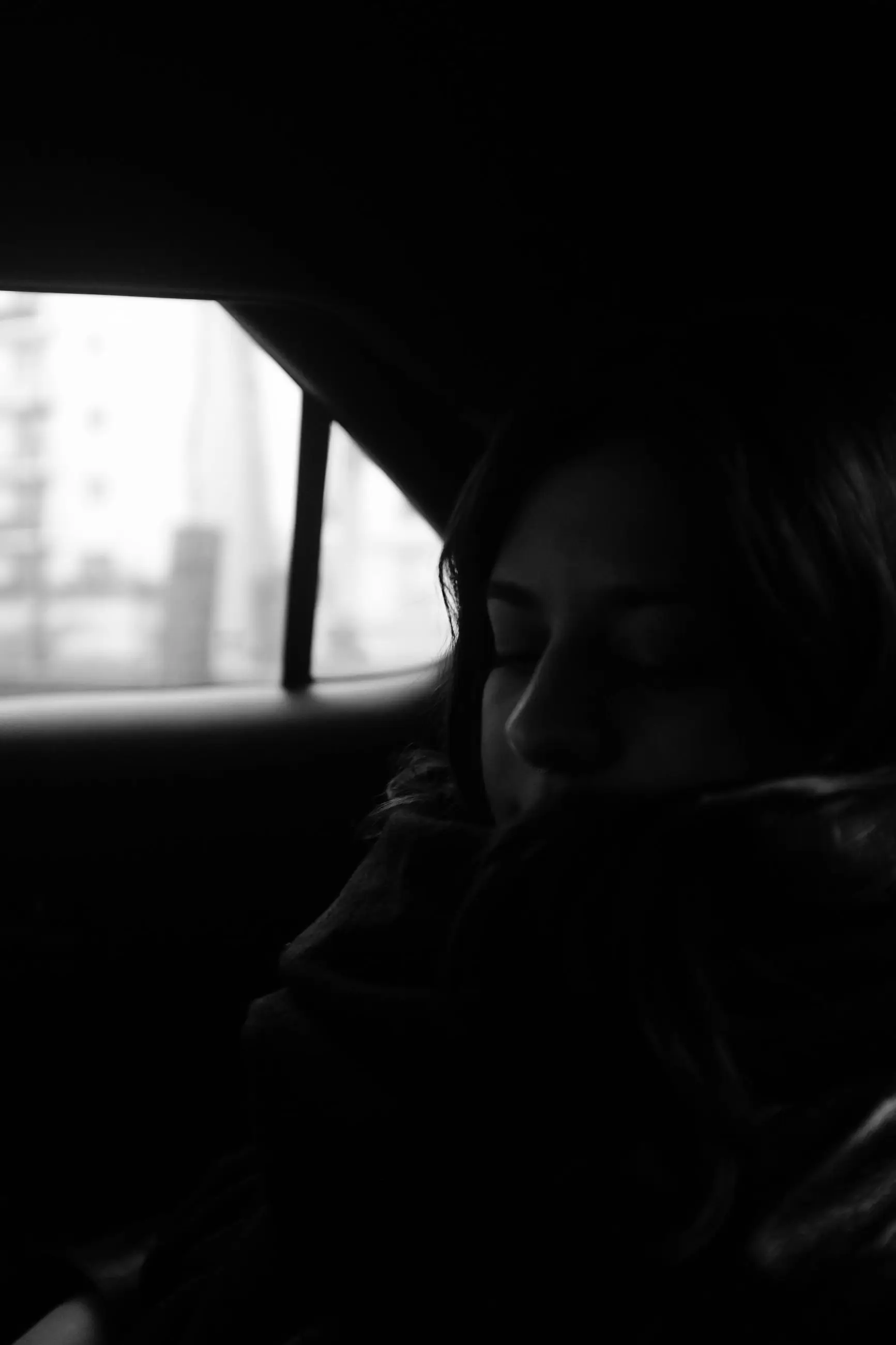 A dark portrait of a woman, one eye catching the window light