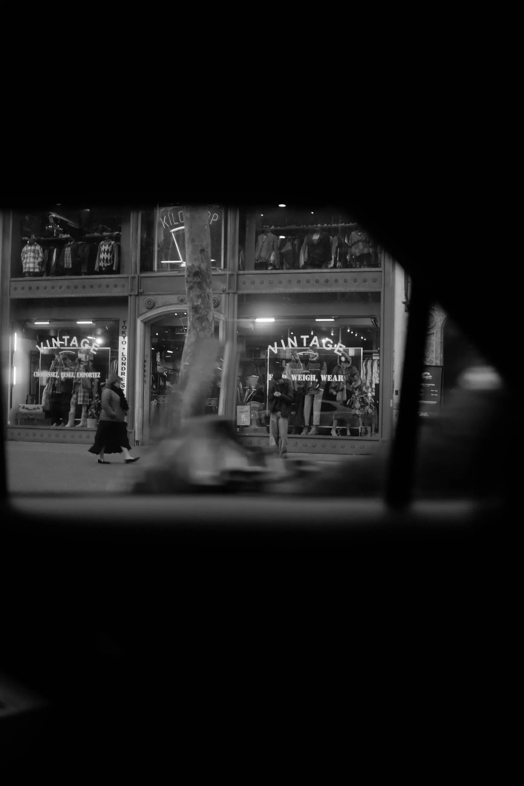 Shop windows lit at dusk, seen through a small opening in the dark