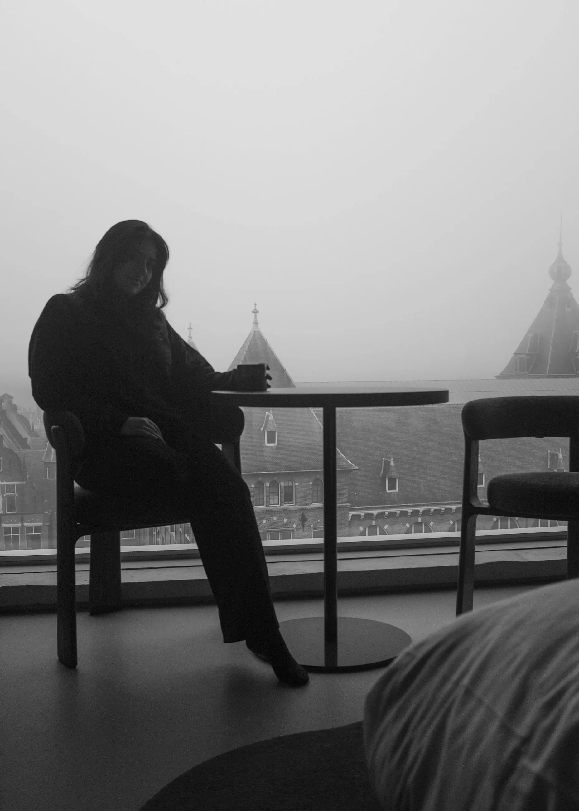 A woman seated with one leg extended, fog beyond the glass