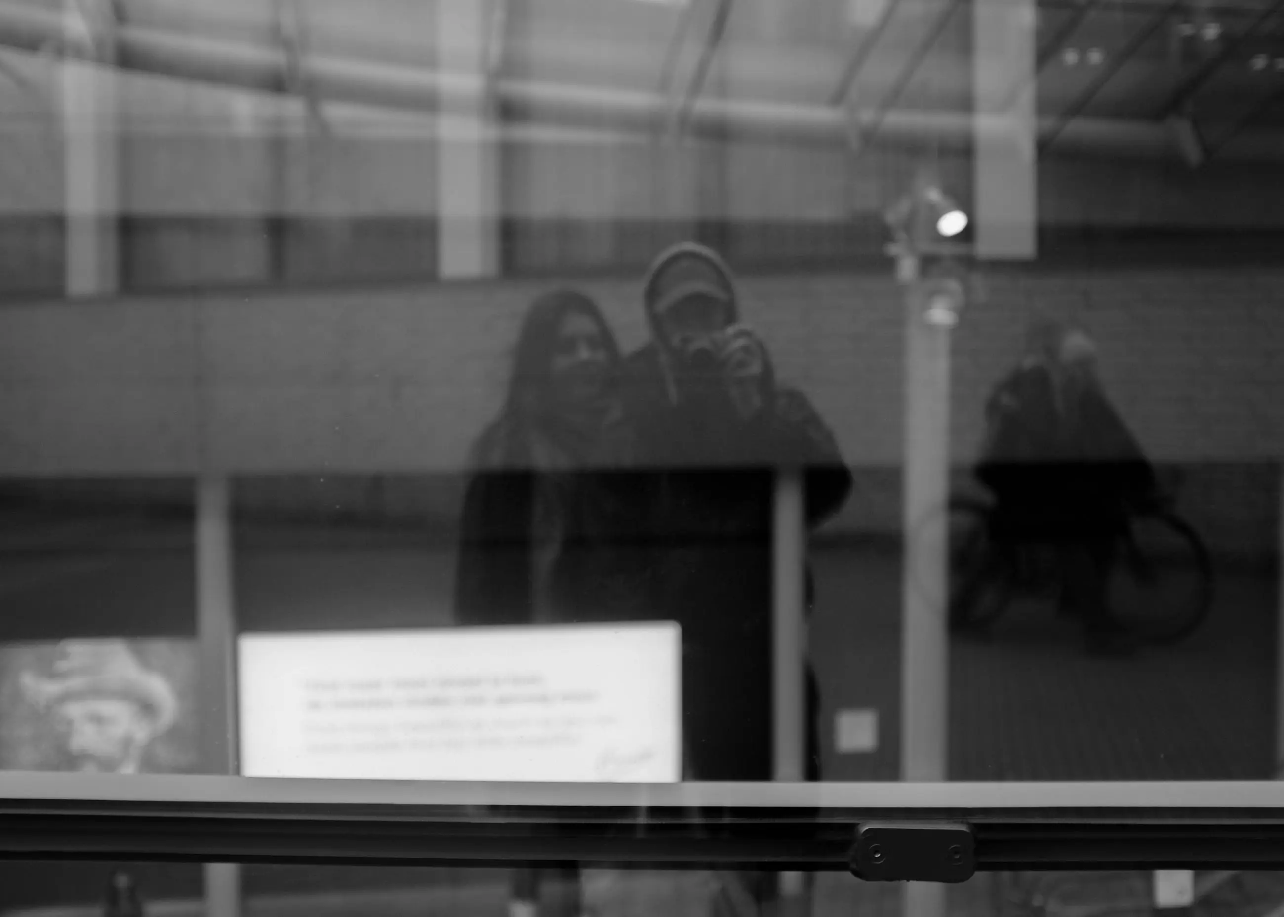 A reflected figure holding a camera in museum glass, a small label lit in the foreground