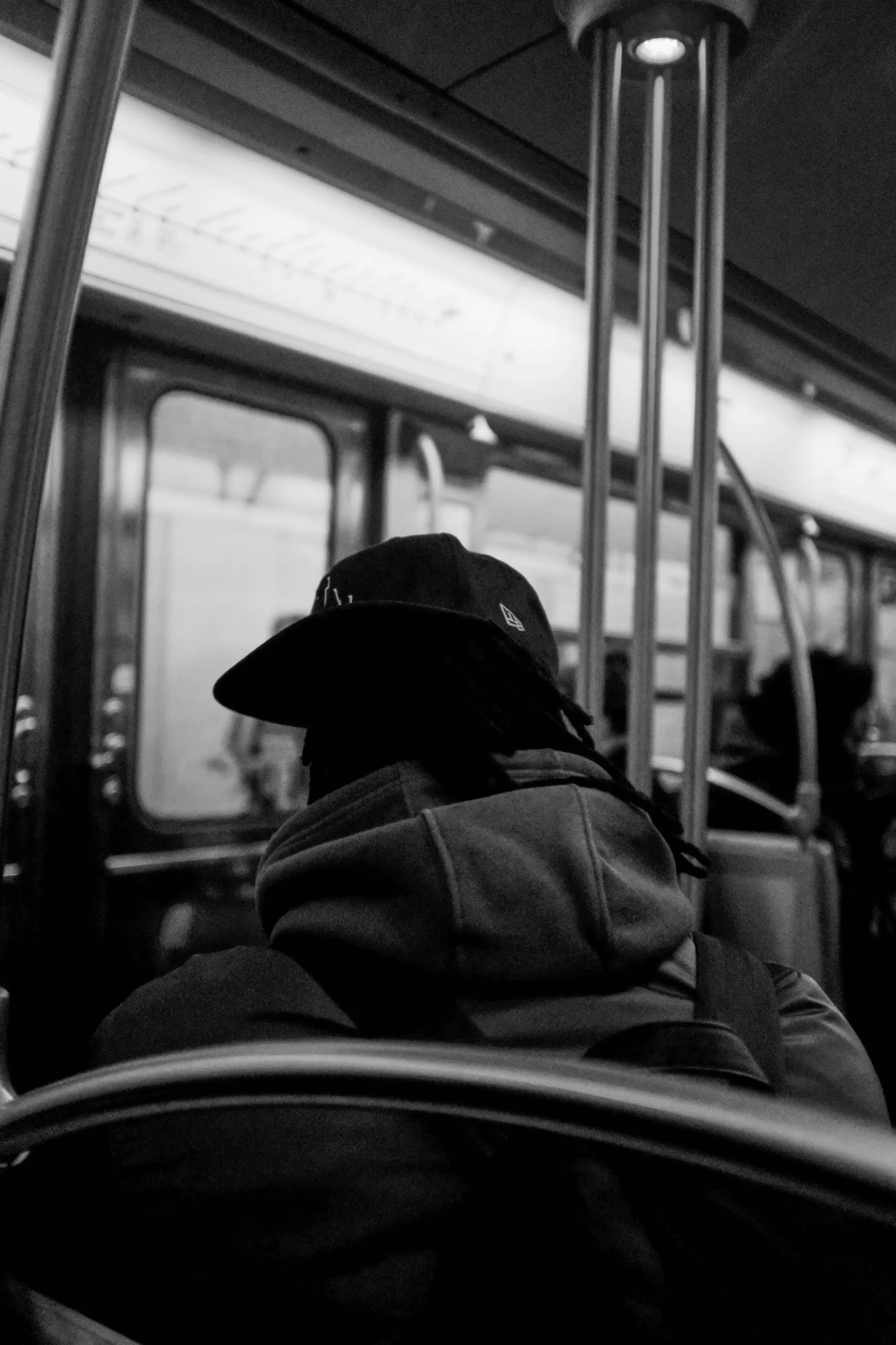 A man in a hat and hooded jacket seen from behind in a metro carriage