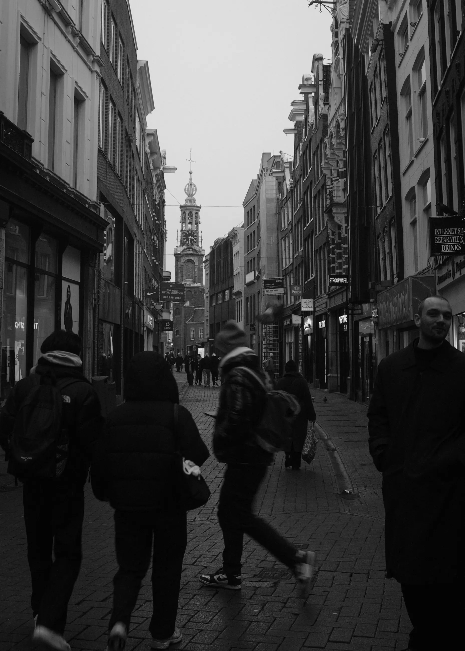 Backs of pedestrians crossing a street, a spire in the distance