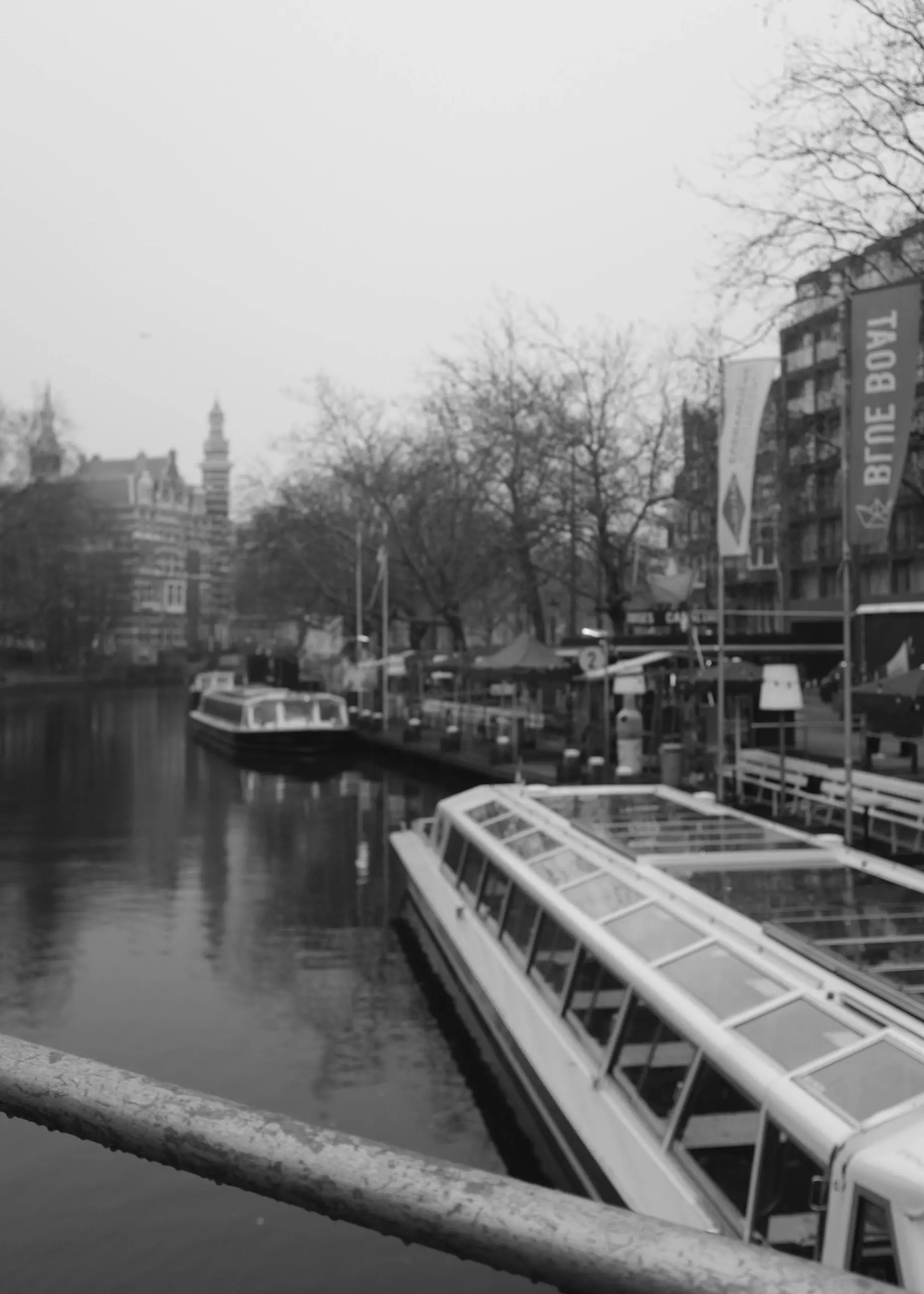 A tour boat moored along a canal under a grey sky, a railing across the frame