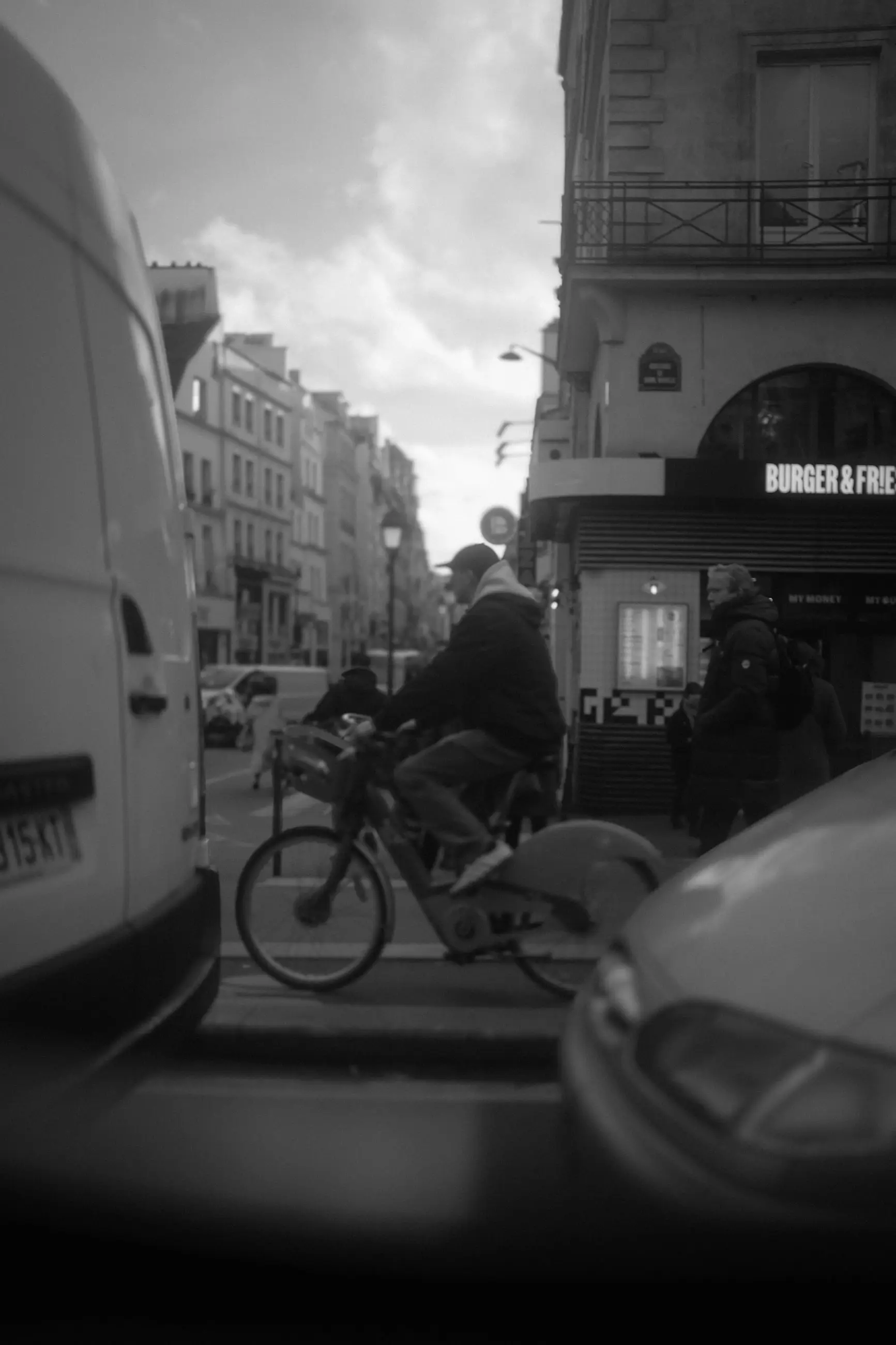A cyclist between two white vans at a street corner