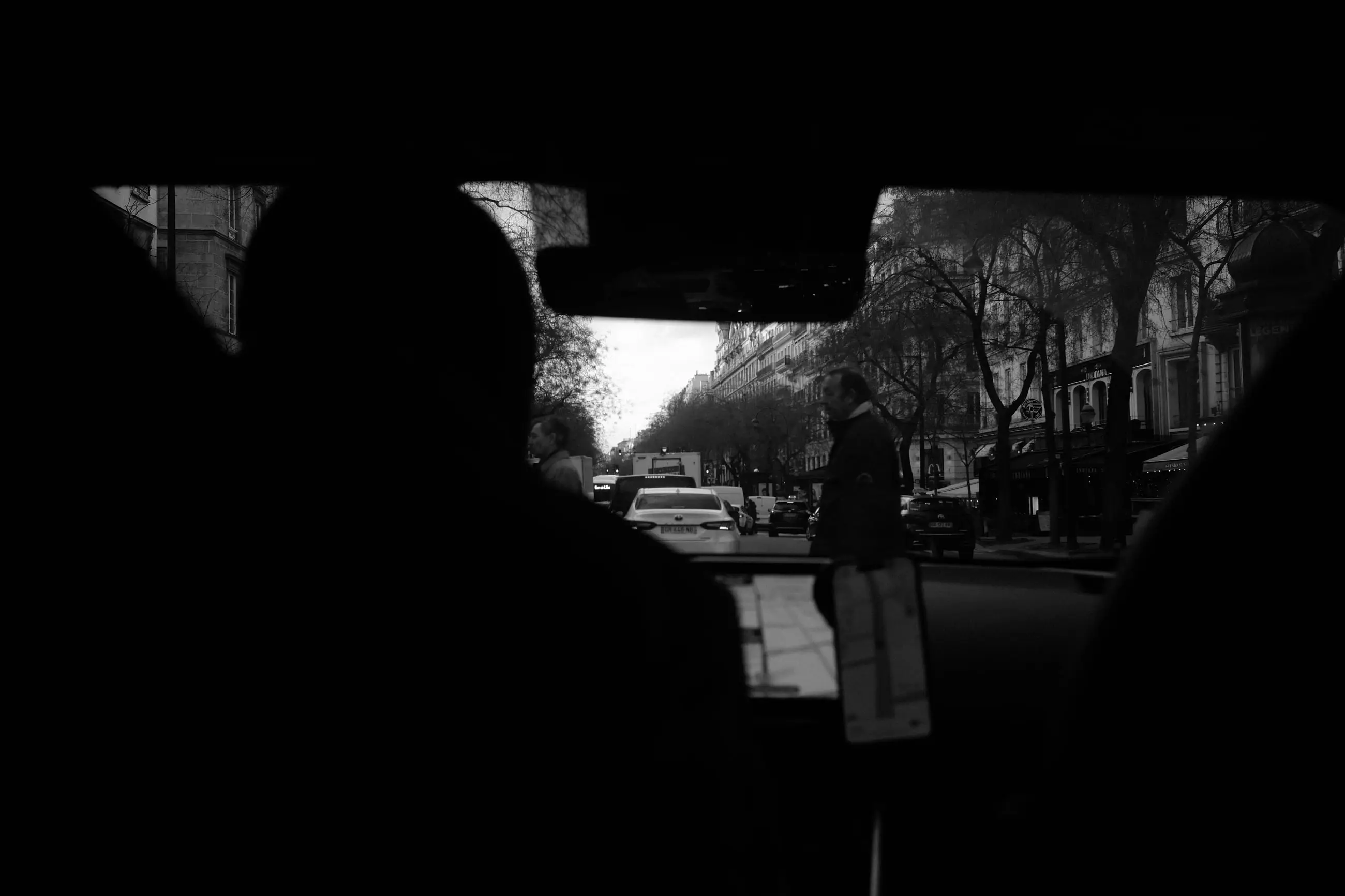 A dark windscreen opening onto a boulevard, a pedestrian waiting at the kerb