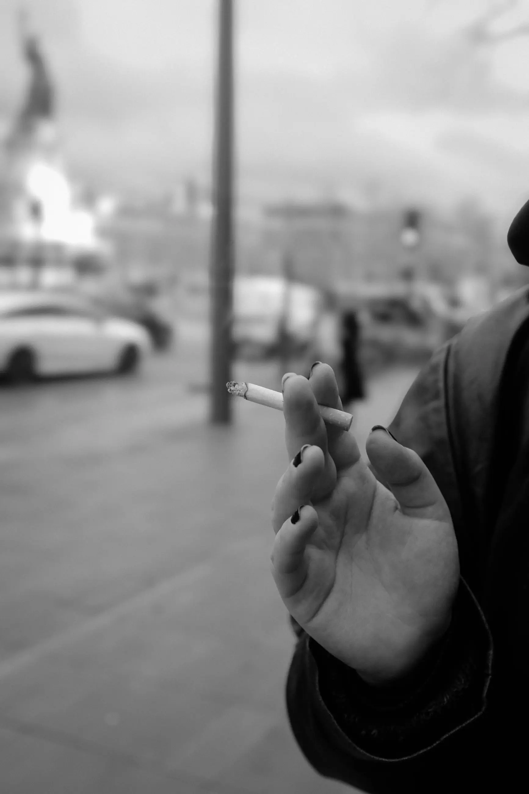 A hand holding a cigarette, the square out of focus behind