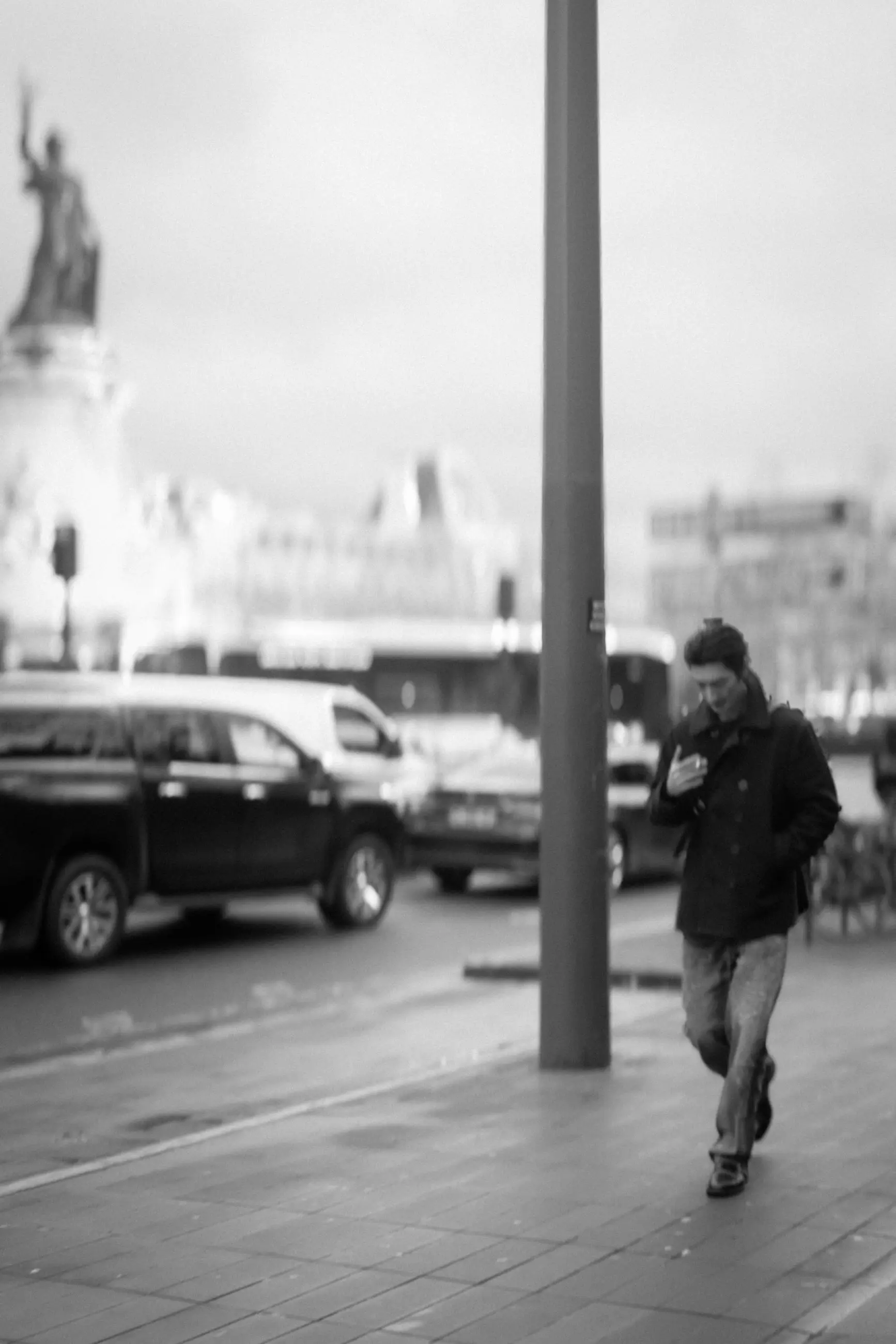 A man in a dark jacket crossing the square, the statue behind him