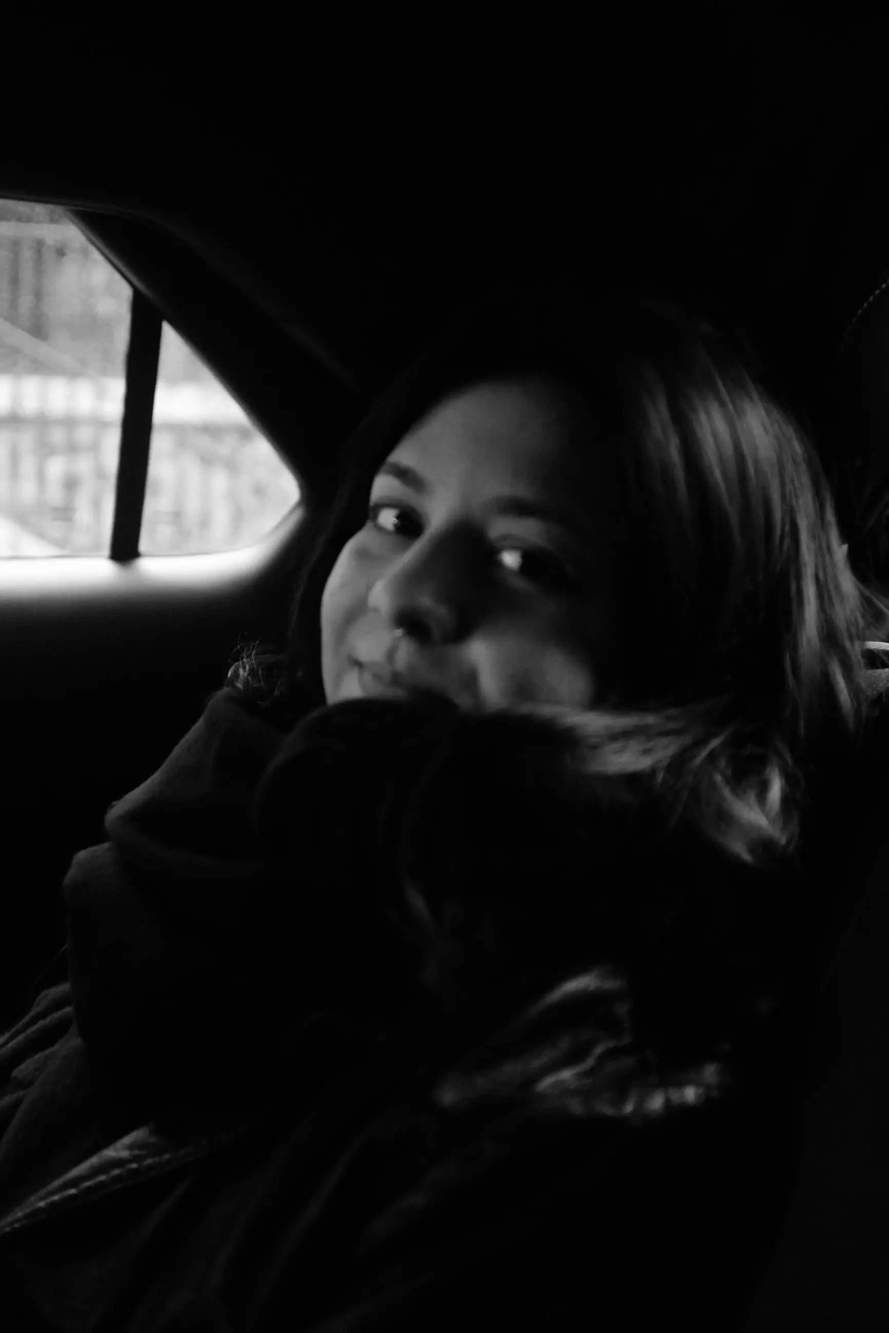 A woman half-smiling over her scarf, the taxi window behind her